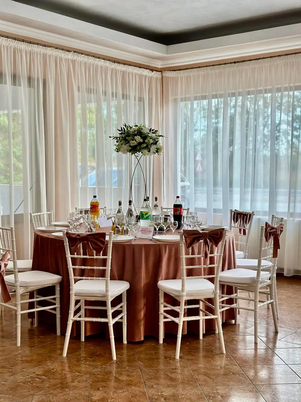 Sala cu mese roz-pudră și aranjamente florale înalte
