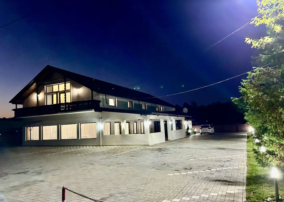 Clădirea Bistro Cafe Events luminată seara, cu parcarea din față